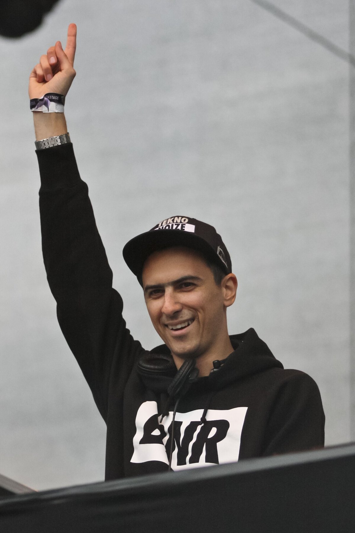 Boys Noize behind the decks in a cap and hoodie, one arm raised, at Juicy Beats festival in 2011